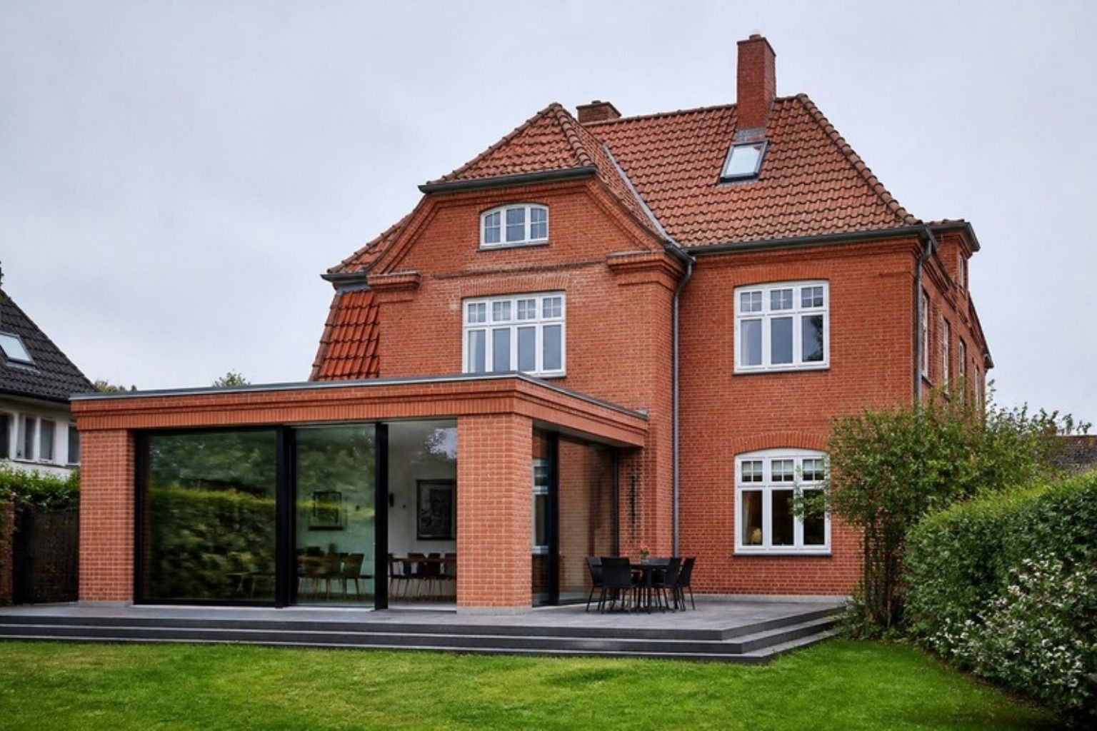 Rød murermestervilla med en ny lav tilbygning i mursten og glas mod haven